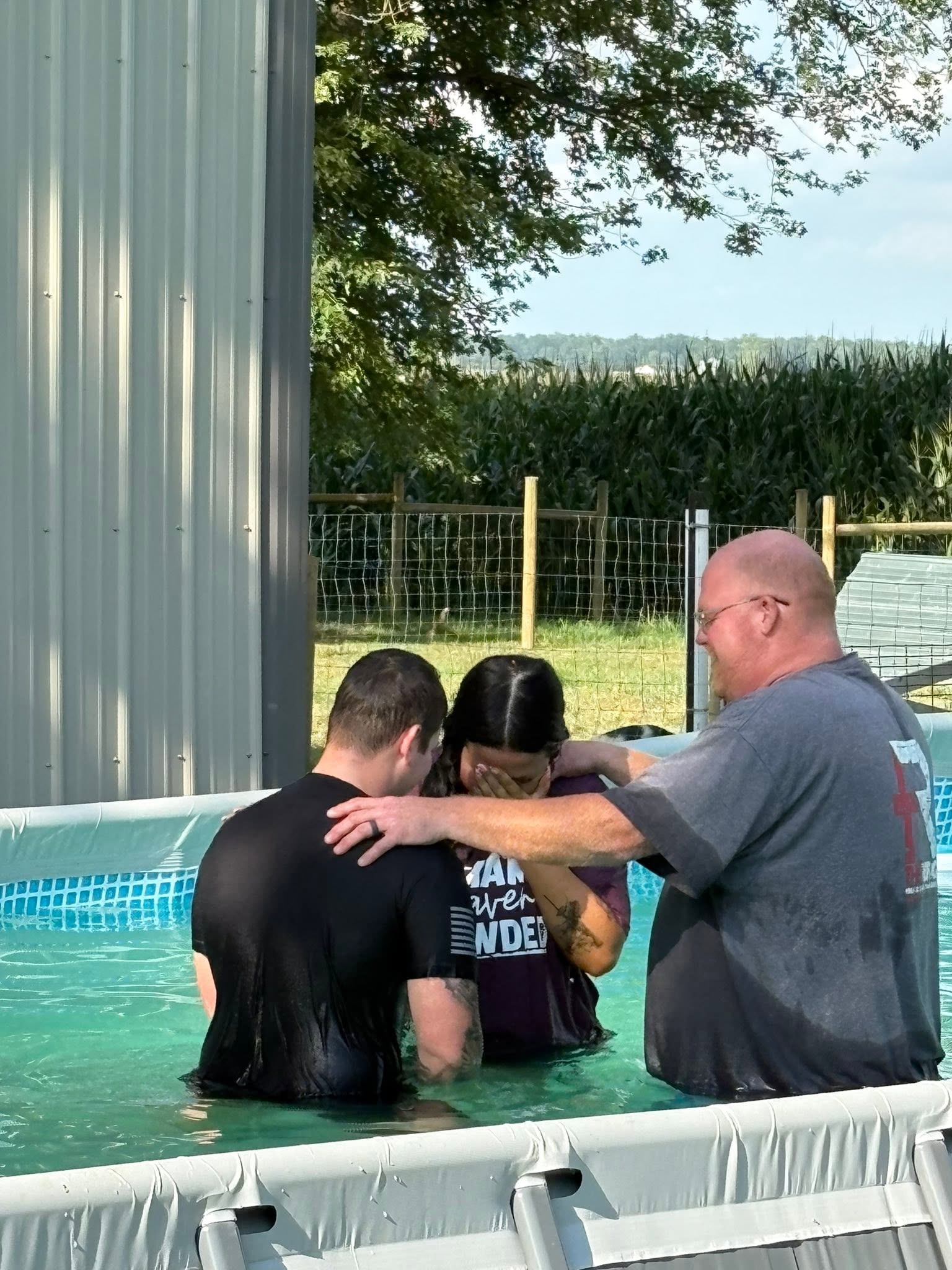 Pastor Bryan and another church leader praying with a person during an outdoor baptism